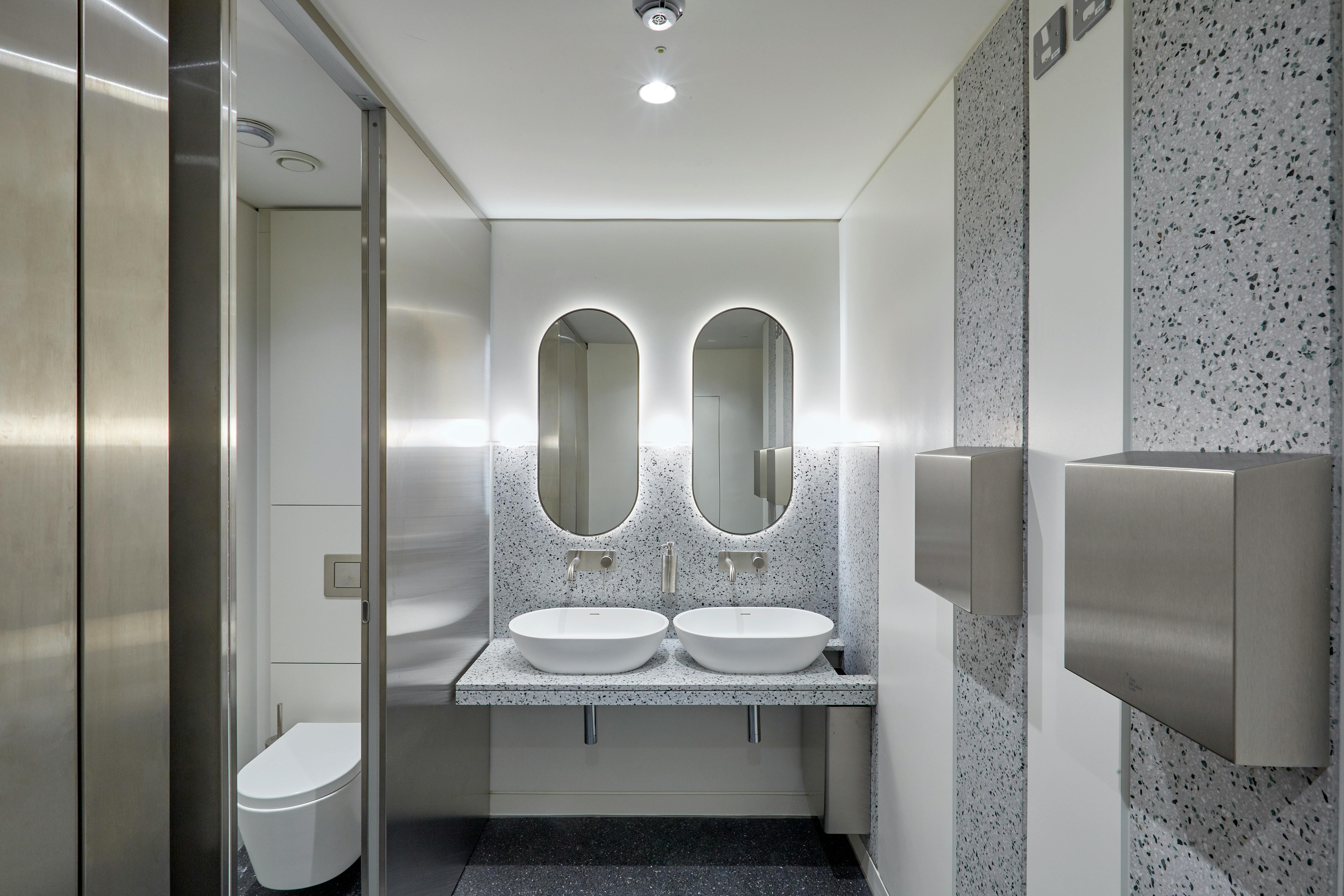 Commercial office washroom with basins, mirrors, cubicle and hand dryer
